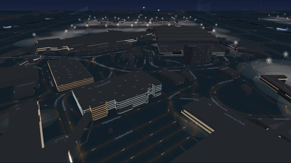 Gebäude in Heathrow bei Nacht: Parkhäuser mit leuchtenden Geschossbändern und ein Hotel mit einzelnen erleuchteten Fenstern, im Hintergrund angestrahlte Abstellpositionen